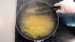 スパゲティを半分に折って加え、くっつかないように混ぜている