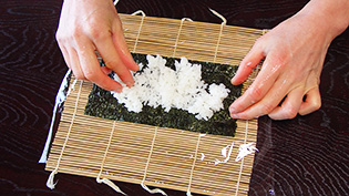 手に酢水をつけ、1/8量の寿司飯をのせて広げている